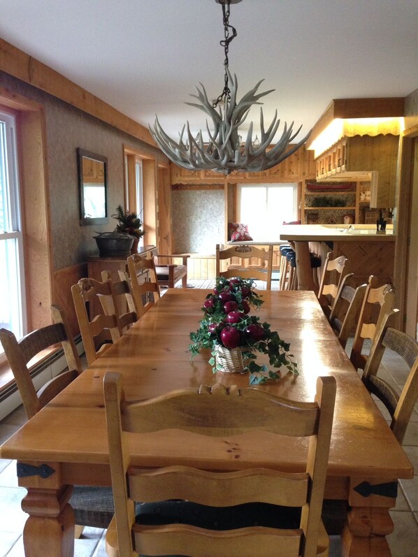 A wooden dining table with chairs, a chandelier, and a Christmas tree centerpiece.