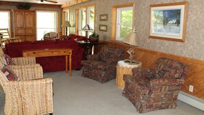 A cozy living room with a red sofa, patterned armchairs, a wooden coffee table, and a ceiling fan.