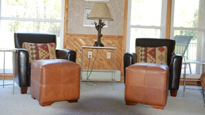 A room with two leather armchairs and ottomans, a table with a lamp, and a fish picture on the wall.