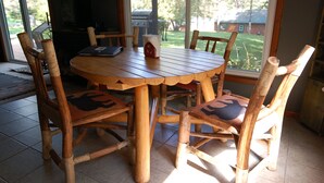 Una mesa de comedor redonda de madera con seis sillas, cada una con un cojín de diseño negro y rojo. La habitación tiene un ventanal con vistas al exterior.