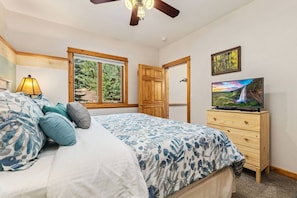 A bedroom with a bed, a dresser, a television, a window, and a door.