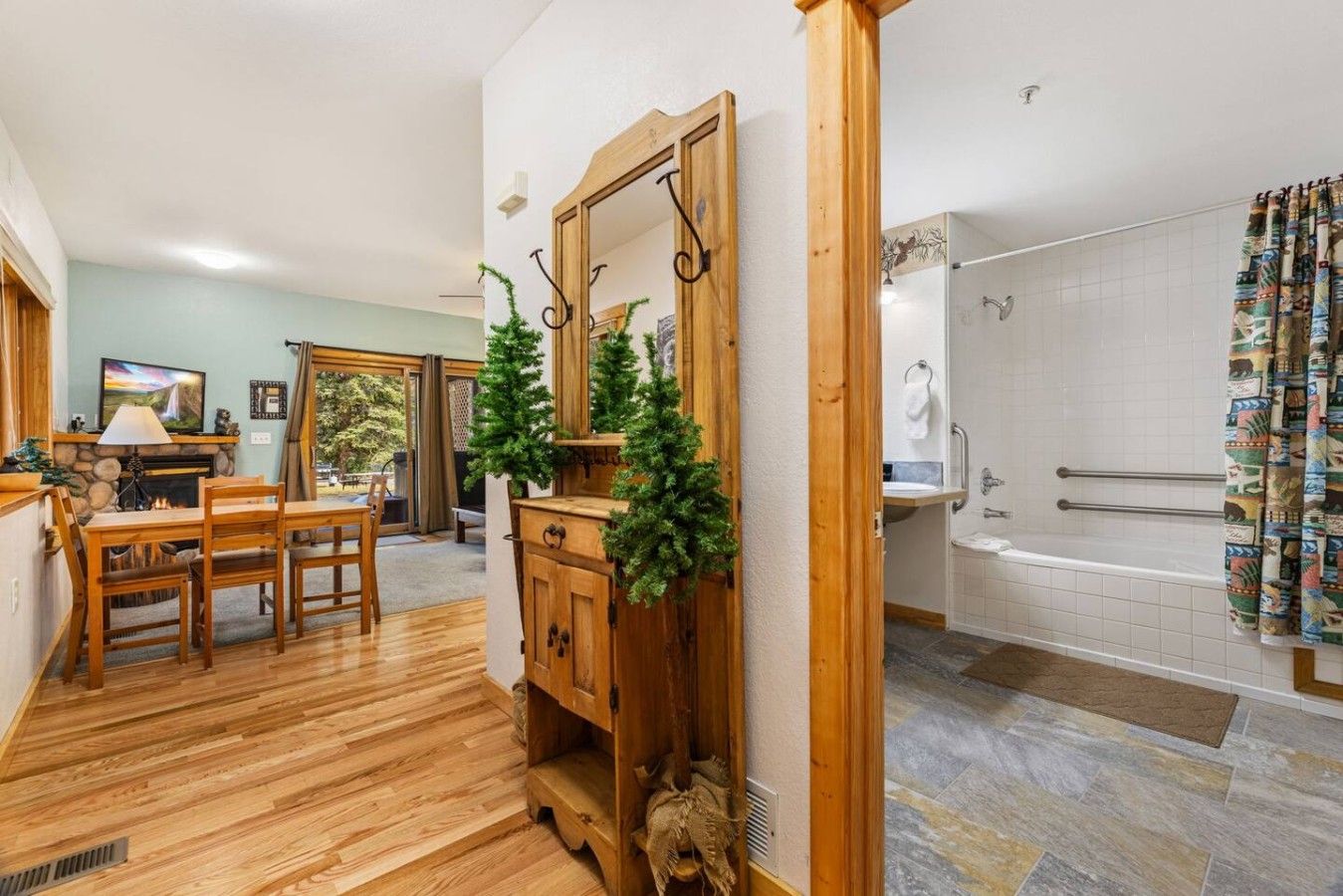 A room with a wooden floor, a fireplace, a dining table with chairs, a mirror, and a bathroom with a bathtub and shower.