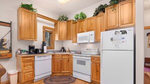 A kitchen with wooden cabinets, a white refrigerator, a microwave, and a stove. There is a rug on the floor and a trash bin. - Fall River Hideaway • Private Hot Tub• Close to RMNP (Estes Park)