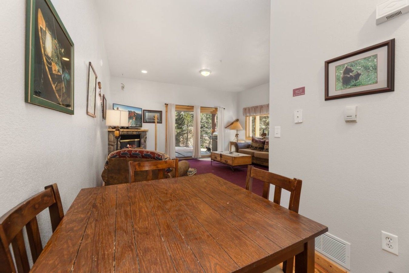 A dining area with a wooden table and chairs, a fireplace, and a view of the outdoors.