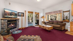 A living room with a stone fireplace, a television, a sofa, and a view of the outdoors. - Fall River Hideaway • Private Hot Tub• Close to RMNP (Estes Park)