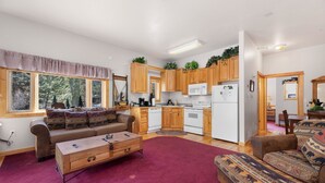 A cozy living room with a sofa, a coffee table, and a rug. There is a kitchen with wooden cabinets and a refrigerator. - Fall River Hideaway • Private Hot Tub• Close to RMNP (Estes Park)
