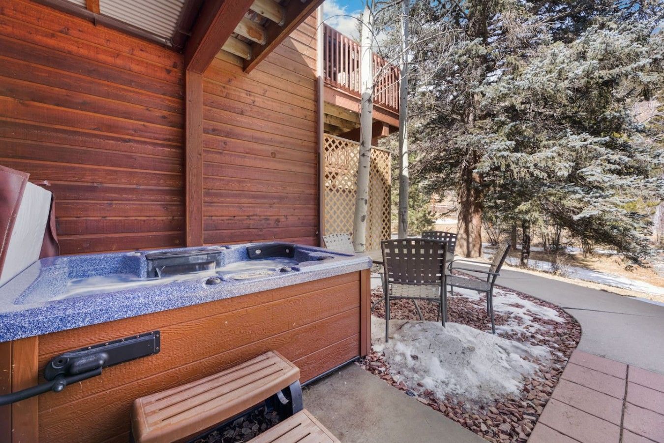 A wooden exterior with a hot tub, a bench, and a chair outside.