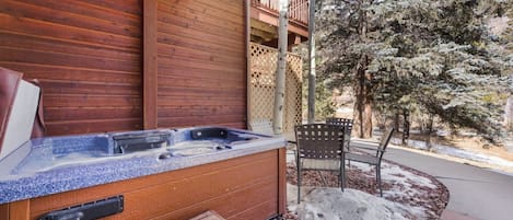 Fachada de madera con jacuzzi, banco y silla en el exterior.