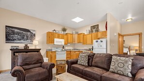 A modern living room with a brown leather sofa, a wooden coffee table, and a kitchen area with wooden cabinets and appliances. - Riverfront Hideaway • Private Hot Tub• Close to RMNP (Estes Park)