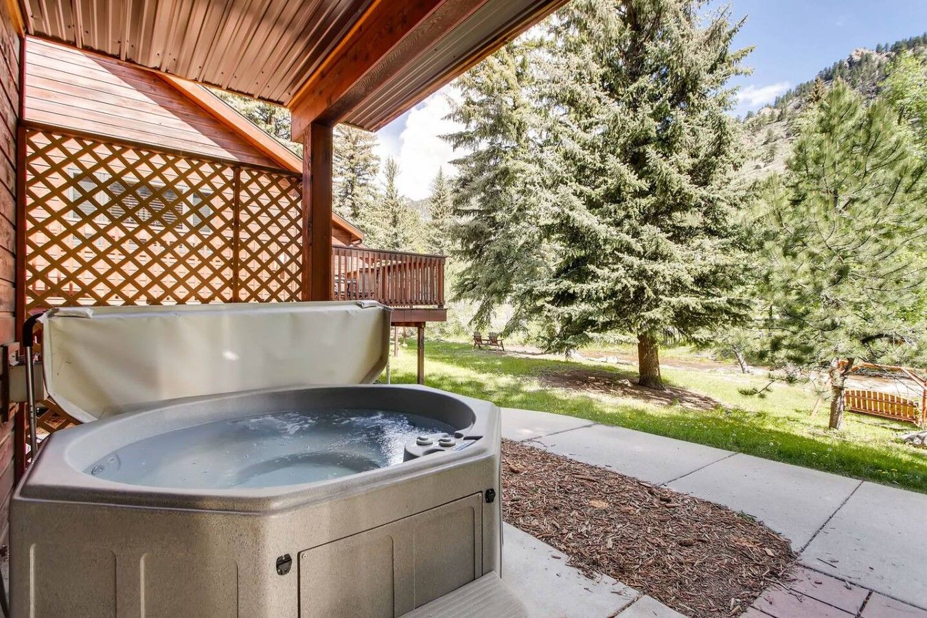 Ein Whirlpool in einem überdachten Außenbereich mit einer Holzterrasse und Blick auf eine bewaldete Landschaft.