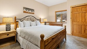 A bedroom with a wooden bed, two bedside tables with lamps, a window with a view of the outdoors, and a wooden door. - Riverfront Hideaway • Private Hot Tub• Close to RMNP (Estes Park)