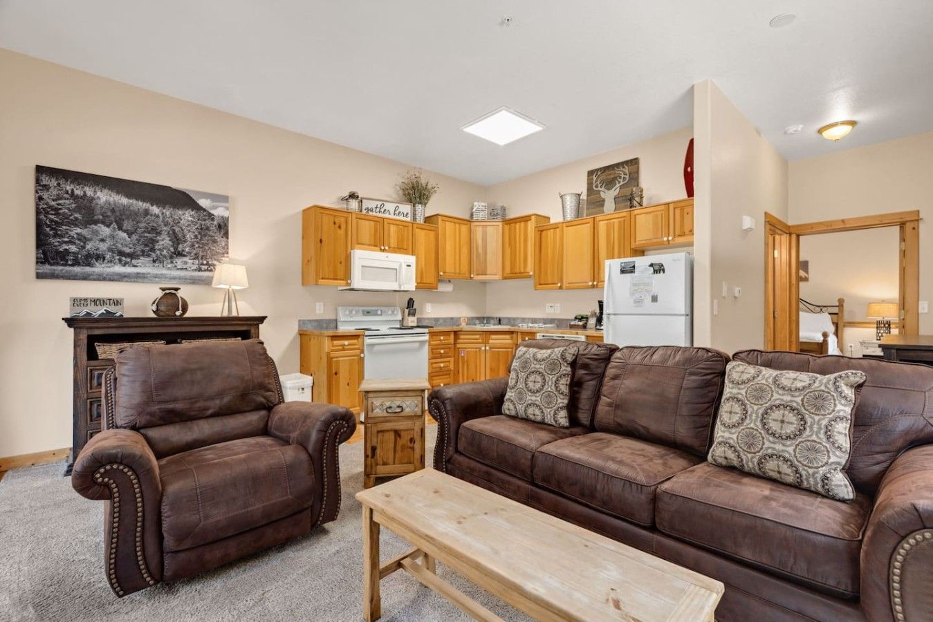 Ein Wohnzimmer mit einer braunen Ledersofa, einem Holztisch und einer Küchenzeile mit Holzschränken und Geräten.