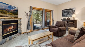 A cozy living room with a stone fireplace, leather furniture, and a scenic view through the glass door. - Riverfront Hideaway • Private Hot Tub• Close to RMNP (Estes Park)