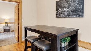 A dining area with a dark wooden table and two leather chairs, a black and white painting on the wall, and a wooden door leading to another room. - Riverfront Hideaway • Private Hot Tub• Close to RMNP (Estes Park)
