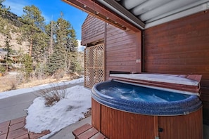 A wooden hot tub with a bench, surrounded by a wooden deck and a view of a snowy landscape with trees.