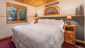 A bedroom with a large bed, wooden ceiling, a window with a view of trees, a nightstand with a lamp, and a sign that says "FAMILY GETAWAY". - Fall River Hideaway • Private Hot Tub (Estes Park)