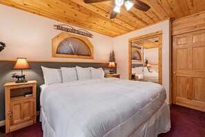 Een hotelkamer met een groot bed, een houten hoofdbord, een plafondventilator, een spiegel en een houten deur.