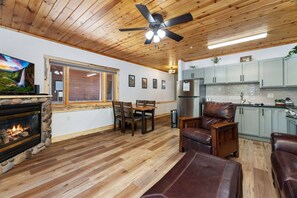 A cozy living room with a fireplace, wooden flooring, a dining area, and a kitchen with light-colored cabinets. - Renovated Fall River Escape • Private Hot Tub (Estes Park)