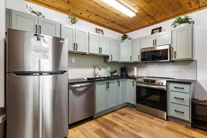 Une cuisine avec des meubles de couleur claire, des appareils en acier inoxydable, un plancher en bois et un plafond avec des poutres apparentes.
