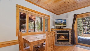 A cozy room with a wooden dining table, chairs, a fireplace, and a television. - Riverfront Escape •Private Hot Tub • Close to RMNP (Estes Park)