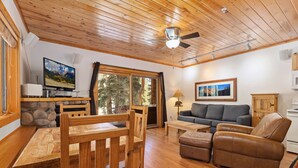 A cozy cabin interior with a wooden ceiling, a stone fireplace, a sofa, a brown leather chair, and a dining table with chairs. - Riverfront Escape •Private Hot Tub • Close to RMNP (Estes Park)