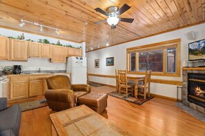 A cozy interior with a wooden ceiling, a dining area with a table and chairs, a fireplace, and a kitchen with wooden cabinets. - Riverfront Escape •Private Hot Tub • Close to RMNP (Estes Park)