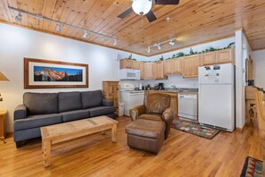 A cozy living room with a sofa, a leather chair, a wooden coffee table, and a ceiling fan.