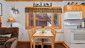 A cozy kitchen with a wooden table, chairs, a microwave, and a stove. - Riverside Fall River Retreat • Private Hot Tub (Estes Park)