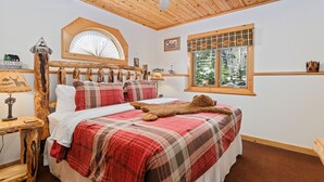 A bedroom with a wooden ceiling, a bed with plaid bedding, a window with a view of trees, and a ceiling fan. - Riverside Fall River Retreat • Private Hot Tub (Estes Park)