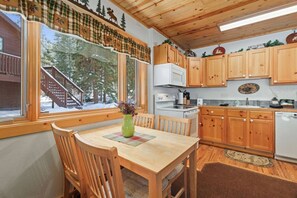 Un interior de madera con una mesa de comedor, sillas, una cocina con armarios de madera, un microondas y una estufa.