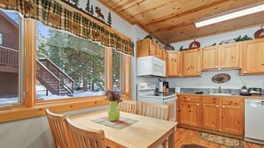 A wooden interior with a dining table, chairs, and a window with a view of trees. - Riverside Fall River Retreat • Private Hot Tub (Estes Park)