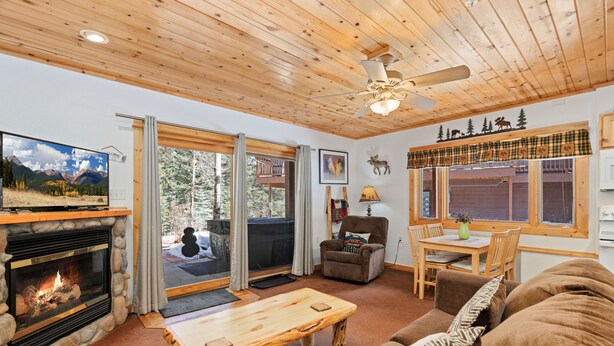 A cozy living room with a fireplace, a wooden ceiling, a television, and a dining area with a table and chairs. - Riverside Fall River Retreat • Private Hot Tub (Estes Park)