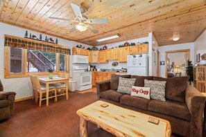 Un interior acogedor con techo de madera, comedor, cocina y sala de estar amoblada con un sofá y una mesa de centro.
