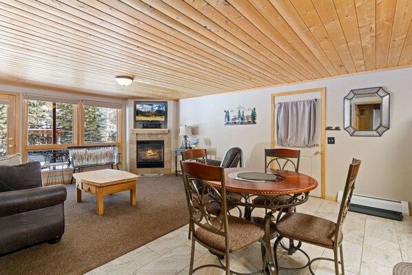A cozy living room with a fireplace, a television, and a dining area with a round table and chairs. - Cozy Fall River Suite • River Views • RMNP (Estes Park)