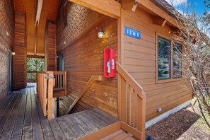 A wooden cabin with a covered porch, a fire extinguisher mounted on the wall, and a sign indicating room numbers 1 & 6. - Riverfront Retreat • Near RMNP • River Views (Estes Park)