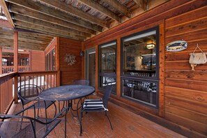A wooden deck with a round table and chairs, large windows, and a hanging fish decoration. - Riverfront Retreat • Near RMNP • River Views (Estes Park)