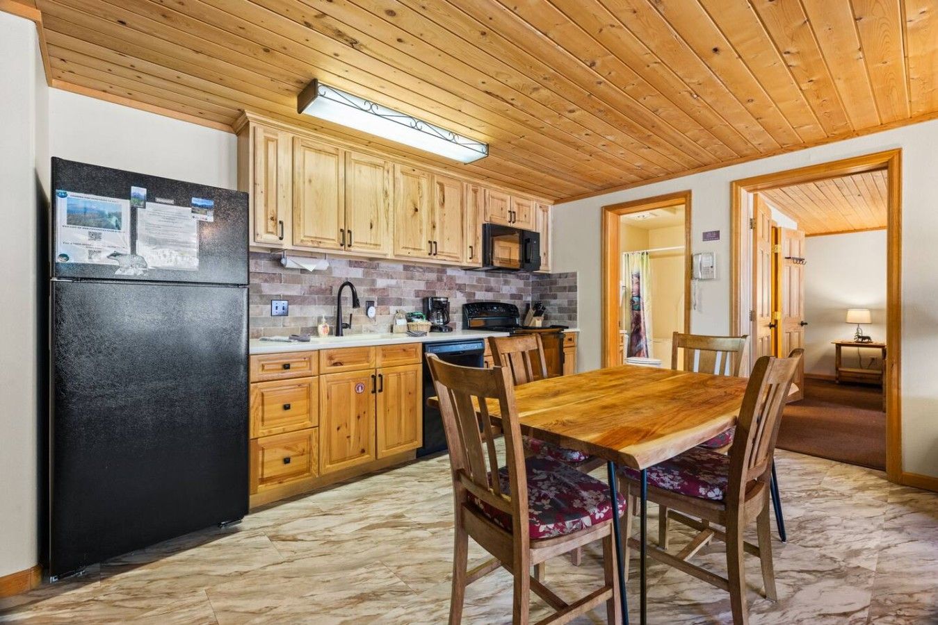 Una cocina con armarios de madera, un refrigerador negro, un microondas y una mesa de comedor con sillas.