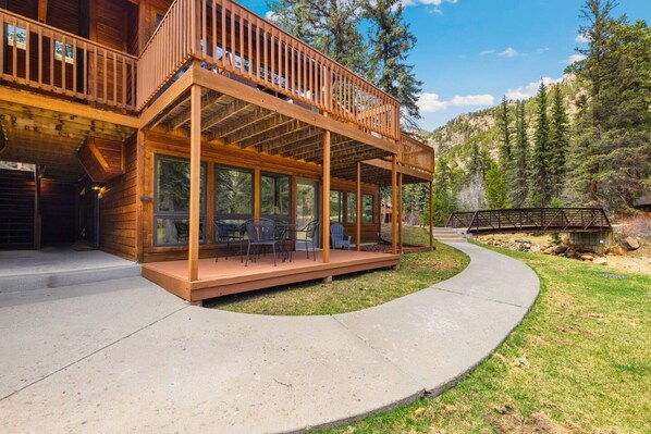 A wooden cabin with a covered porch, outdoor seating, and a view of a forested mountain.