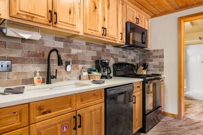 A kitchen with wooden cabinets, a black dishwasher, and a tiled backsplash.