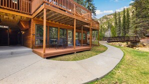Une cabane en bois dotée d’un balcon et de grandes fenêtres, entourée d’un paysage boisé.
