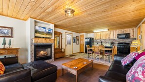 Un salon chaleureux avec une cheminée, des canapés en cuir, une table basse en bois et un coin cuisine doté de meubles en bois et d’un four à micro-ondes.