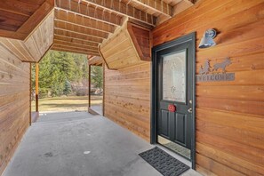 A wooden cabin entrance with a black door, a welcome sign, and a number plaque.
