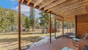 A wooden deck with outdoor furniture, overlooking a forested area with a clear sky. - Quiet Fall River Suite • River Views • RMNP (Estes Park)