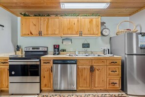 A kitchen with wooden cabinets, stainless steel appliances, a clock, and a basket on the wall.