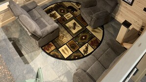 Interior acogedor de una cabaña con dos sofás grises, un ventanal grande, un televisor montado y un mapa enmarcado en la pared.