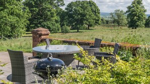 Une terrasse extérieure aménagée avec des meubles en osier, une table à plateau en verre et un barbecue noir.