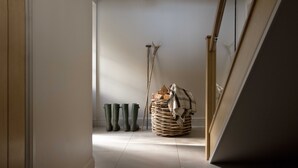Un couloir avec un panier en osier rempli de bois de chauffage et une couverture, ainsi que quatre bottes vertes appuyées contre le mur.