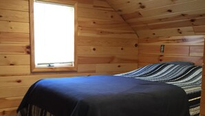 Habitació d'una cabana de fusta amb un llit, una finestra i una làmpada al sostre.
