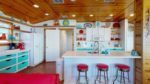 Een keuken met houten plafond, witte kasten, een centraal eiland met krukken, en diverse decoratieve objecten.