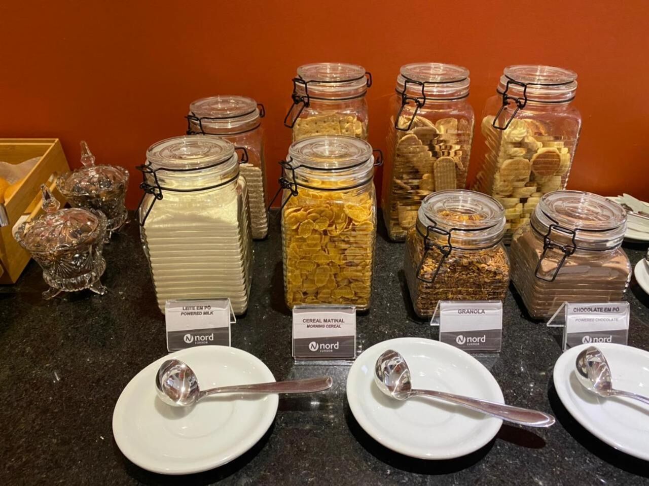 Een ontbijtbuffet met diverse cornflakes en granola opties in glazen potten, elk voorzien van het merk 'Nord'.
